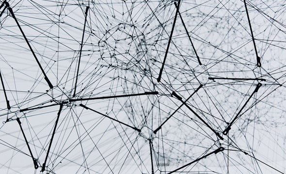 Black and white photograph of a complex web made of medal wires come in and out of various central nodes