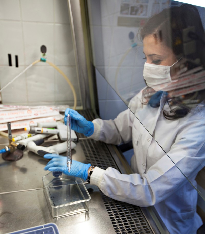 Woman in lab clothes wearing protective mask conducting tests in laboratory setting