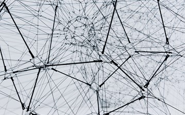 Black and white photograph of a complex web made of medal wires come in and out of various central nodes