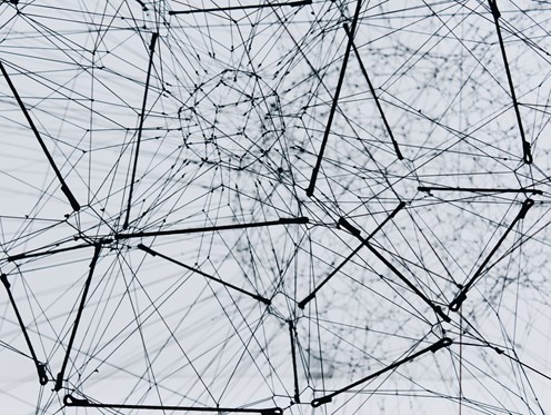 Black and white photograph of a complex web made of medal wires come in and out of various central nodes