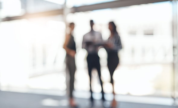 Blurred image of three professionals, one mand and two women, in office clothes standing up 