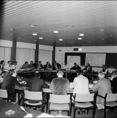 Black and white photo of men sitting around a circular table in a meeting room